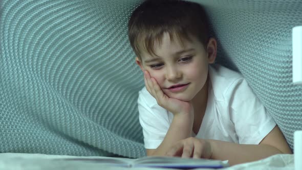 a Seven-year-old Boy Reads a Book Under a Blanket