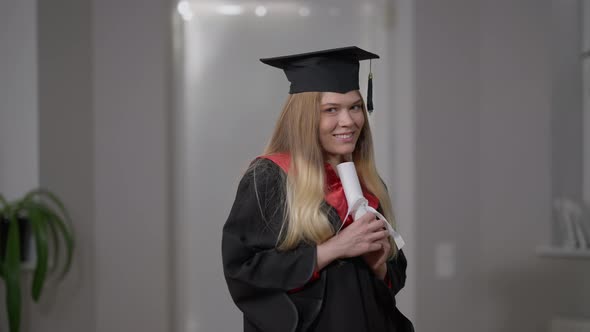 Medium Shot Happy Woman in Graduating Gown and Cap Hugging Rolled Diploma with Ribbon Smiling