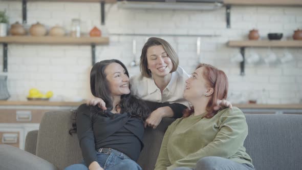 Charming Slim Woman Hugging Friends Sitting on Couch and Talking