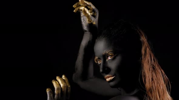 Portrait of a Young Woman with Black Paint on Her Face and Golden Hands and Lips