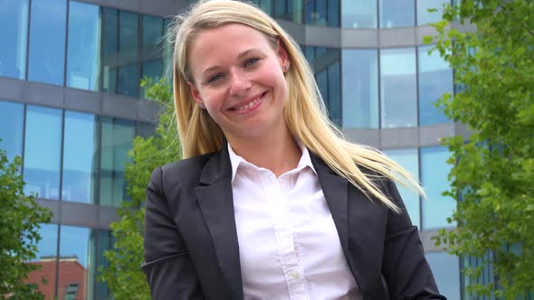 A Young Beautiful Businesswoman Smiles at the Camera - Closeup From Below - an Office Building