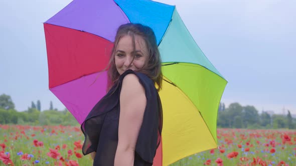 Portrait Attractive Girl Under Colorful Umbrella Spinning and Dancing in a Poppy Field Smiling