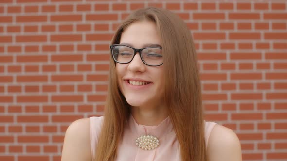 Portrait of a Girl Student Wearing Glasses That Laughs and Smile Against a Brick Red Wall