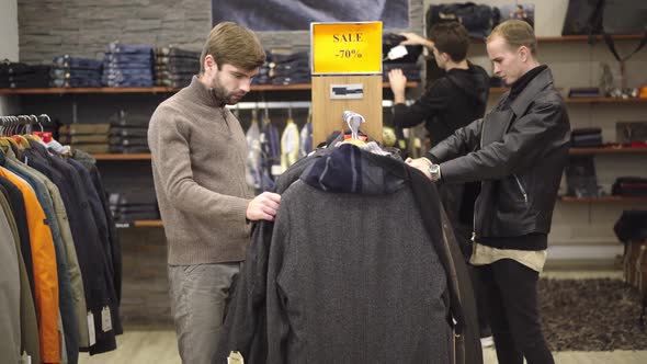 Young Caucasian Men Choosing Clothes in Shop During Black Friday Sales. Three Concentrated Handsome