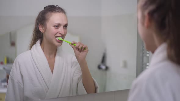 Reflection in Mirror of Young Slim Brunette Caucasian Woman Brushing Teeth with Toothbrush and