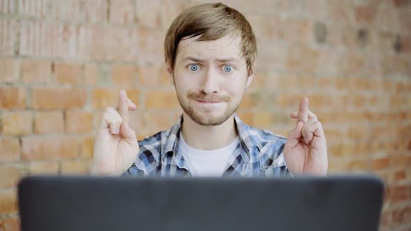 Young man in front of the laptop with his fingers crossing, Crossed fingers symbolizing good luck