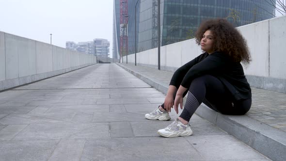 Plus size sportive young woman sitting on the ground in the city