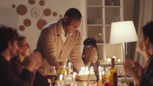 Joyous Afro-American Woman Blowing Candles on Birthday Cake at Dinner Party