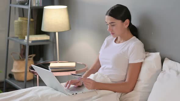 Latin Woman Online Shopping Success on Laptop in Bed