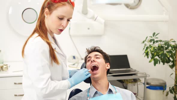 Young Female Dentist Examining Teeth of Male Patient with Mouth Mirror During Checkup