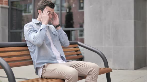 Stressed Casual Young Man with Headache Sitting Outdoor