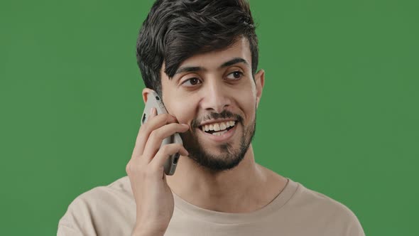 Close Up Happy Smiling Young Arab Guy in Studio on Green Background Talking Using Smartphone