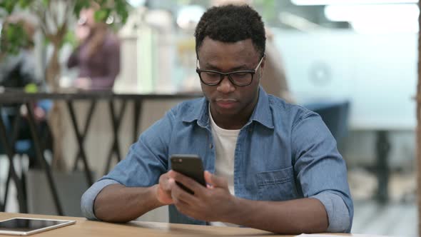 Attractive Young African Man Using Smartphone in Modern Office