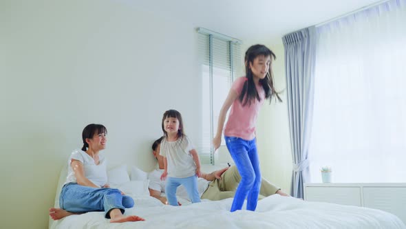 Loving couple enjoy look to young little girl daughters playing and jumping on bed together at home.