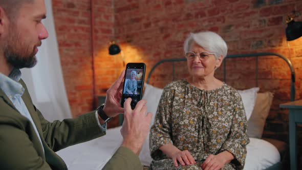 Middleage Caucasian Entrepreneur Taking Photo of His Elderly Greyhaired Mother with His Smartphone