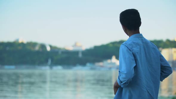 African American Guy Resting on River Embankment Enjoying City View, Landscape