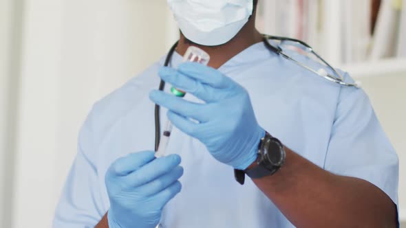 Video of african american male doctor in face mask preparing vaccine