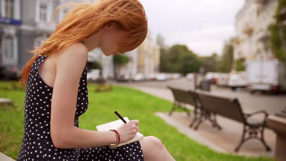 Charming Caucasian Young Redhead Girl with Freckles Writing Notes Wearing Black Polka Dot Dress