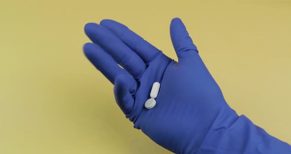 One Oval and One Round White Pills in Hand Dressed in Blue Medical Glove