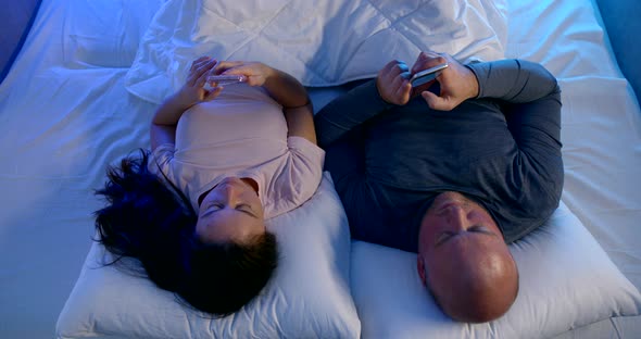 A Married Love Couple: a Bald Man and a Dark-haired Woman Are Lying on a Bed on White Bed Linen