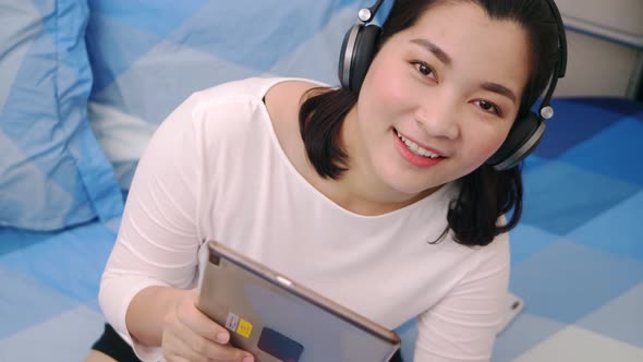 Beautiful asian woman look camera and smile relaxing and listening to music by tablet with headphone