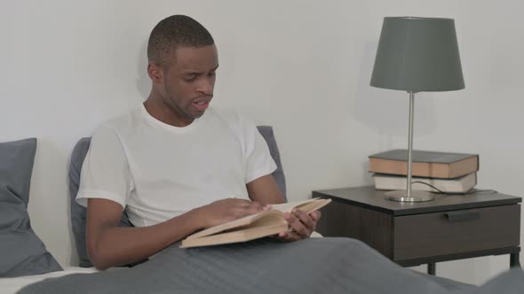 African Man Reading Book While Sitting in Bed