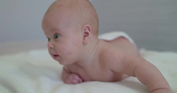 Portrait of Cute Baby Boy Looks Around on Bed with Smile