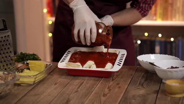 Closeup View of a Young Cook Standing at the Wooden Table and Pouring Tomato Sauce on Enchilada