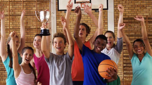 High school kids cheering while holding trophy in basketball court