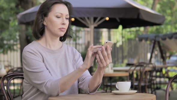 Old Woman Upset By Loss on Smartphone Sitting in Outdoor Cafe