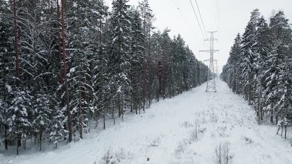 Flying Under Power Lines with Tower in Winter Snowy Forest
