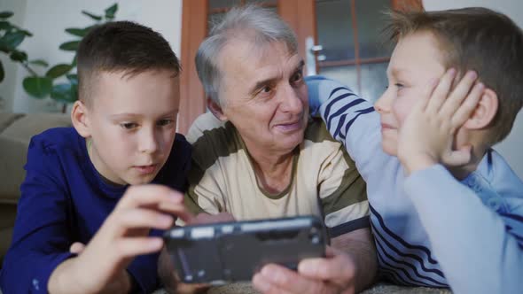 Senior grandfather and a small grandchildren playing game on smartphone at home. Family idyll.