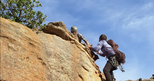 Man helping his friend to climb a cliff