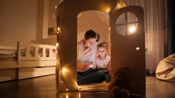 Happy Family with Little Son Playing in Tent or Toy House at Night and Using Tablet Computer