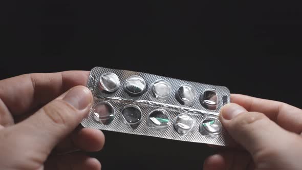 Man's Hand Holds an Empty Medicine Blister on a Dark Background, Close-up