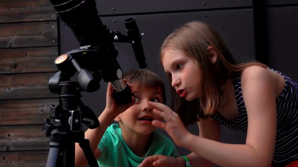 A Cute Girl and Her Little Brother are Looking Through a Telescope at the Sky