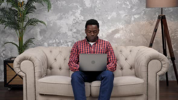 Smiling African American Man Sitting on Couch Work for Laptop Typing on Keyboard