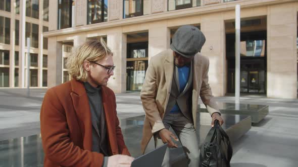 Two Multiethnic Businessmen Speaking and Using Laptop Outdoors