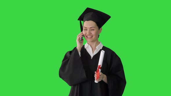 Emotional Female Student in Graduation Robe Talking on the Phone Holding Diploma on a Green Screen