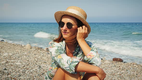 Charming woman in summer hat sitting on beach at windy day