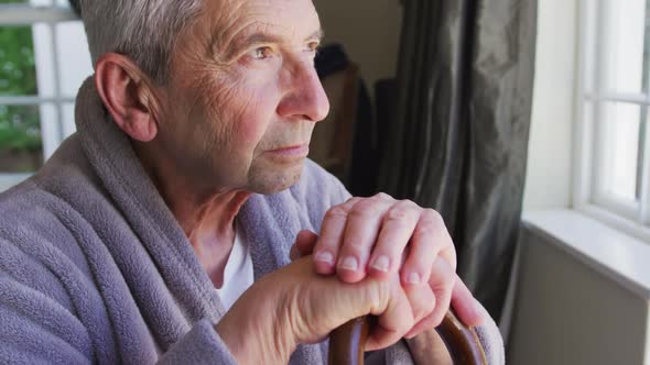 Sad senior caucasian man wearing bathrobe sitting by window