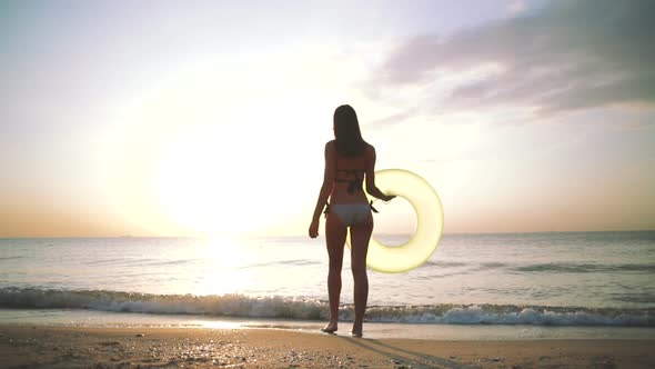 Beautiful Young Woman Standing with Colorful Inflatable Ring at Sea Coast During Sunset Slow Motion