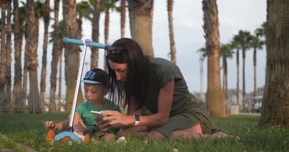 Young Mother and Little Son on the Grass in a Tropical Park Among Palm Trees. Happy Family Concept.