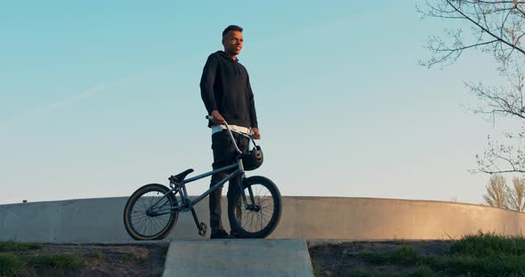 Handsome Bmx Boy Standing on Ramp Holding Bike and Helmet in Hand Dressed All in