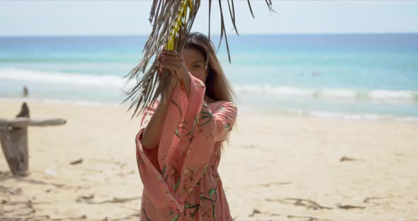 Cheerful Ethnic Female Standing Near Palm on Beach