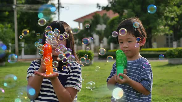 Cute Asian Children Shooting Bubbles From Bubble Gun In The Park