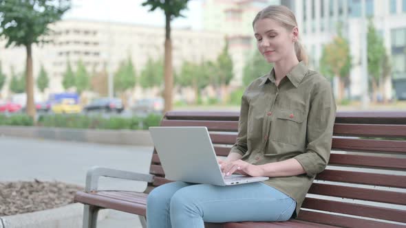 Agree Woman Pointing at Camera while Sitting on Bench Outdoor