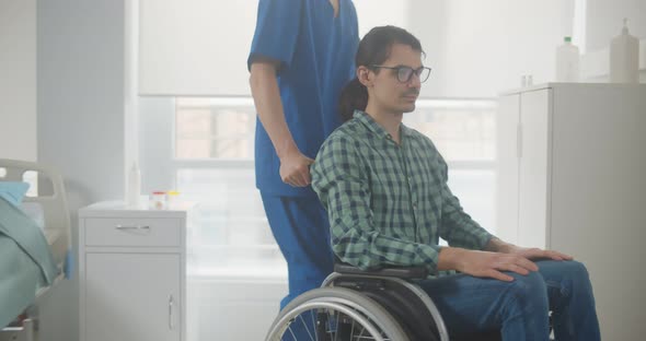 Nurse Taking Young Man Patient in Wheelchair at Hospital Ward