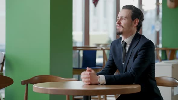 Happy Handsome Bearded Young Man with Mustache Sitting in Cafe Looking Away and Smiling