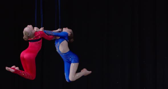 Two Girls in Red and Blue Costumes Spinning in the Air Above Stage Gymnastics